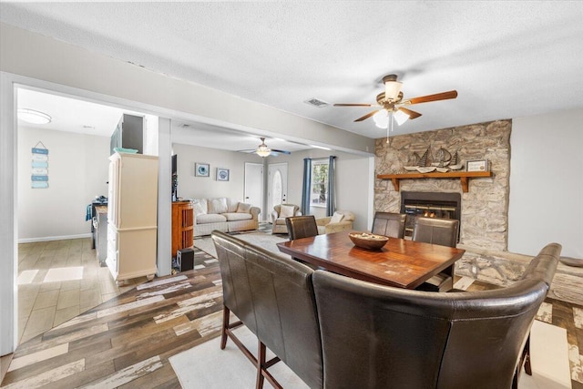 dining room with ceiling fan, a fireplace, a textured ceiling, and hardwood / wood-style floors