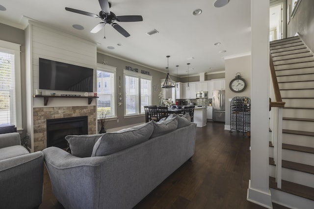 living room with a fireplace, crown molding, dark wood-type flooring, and ceiling fan