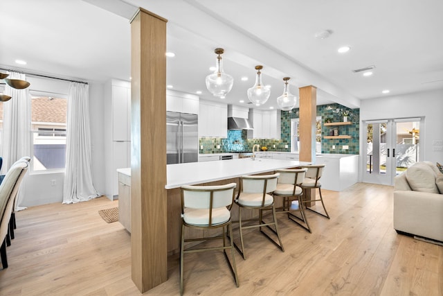 kitchen featuring white cabinetry, built in fridge, hanging light fixtures, wall chimney range hood, and a breakfast bar