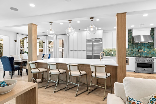 kitchen featuring white cabinetry, wall chimney exhaust hood, high quality appliances, and pendant lighting