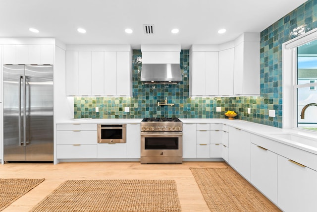 kitchen with tasteful backsplash, high end appliances, wall chimney exhaust hood, white cabinets, and sink