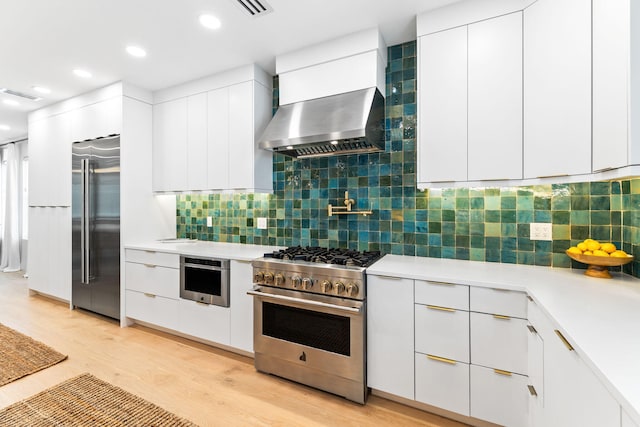 kitchen with decorative backsplash, wall chimney range hood, high end appliances, and white cabinetry