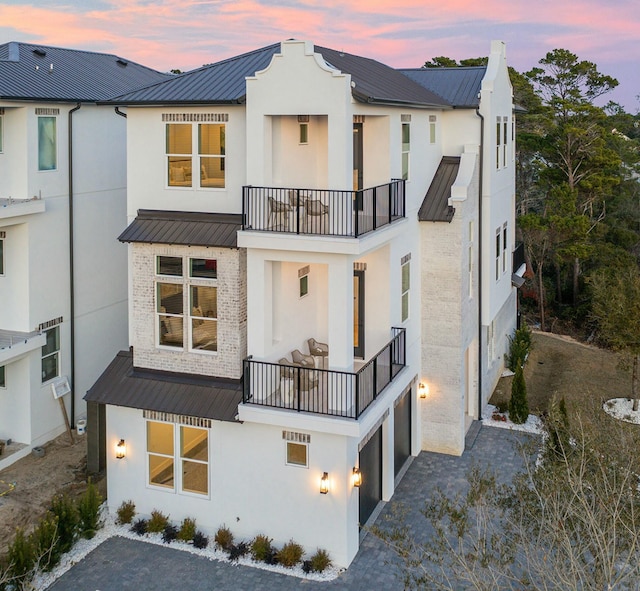 back house at dusk featuring a balcony and a garage