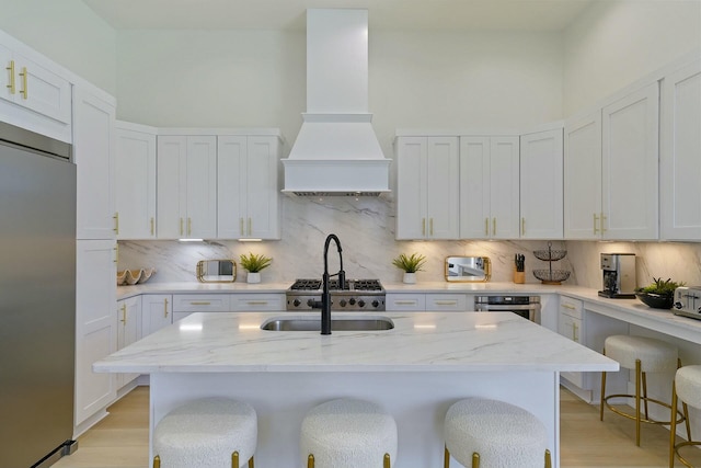 kitchen featuring a kitchen breakfast bar, appliances with stainless steel finishes, custom exhaust hood, backsplash, and light stone counters