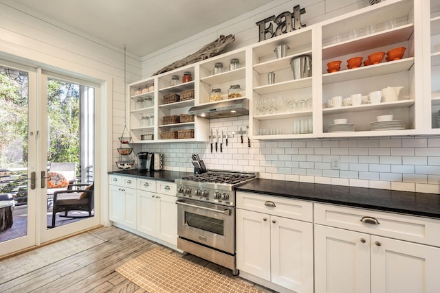 kitchen with high end range, backsplash, white cabinetry, light hardwood / wood-style floors, and wooden walls