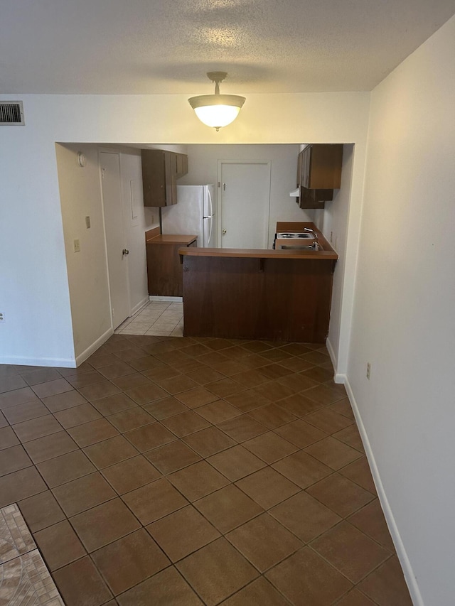 kitchen with light tile patterned flooring, kitchen peninsula, white fridge, and a textured ceiling