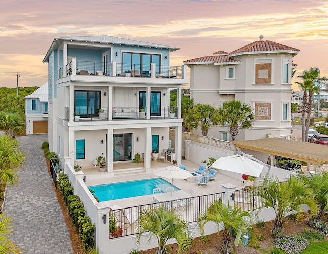 back house at dusk featuring a balcony, a fenced in pool, and a patio