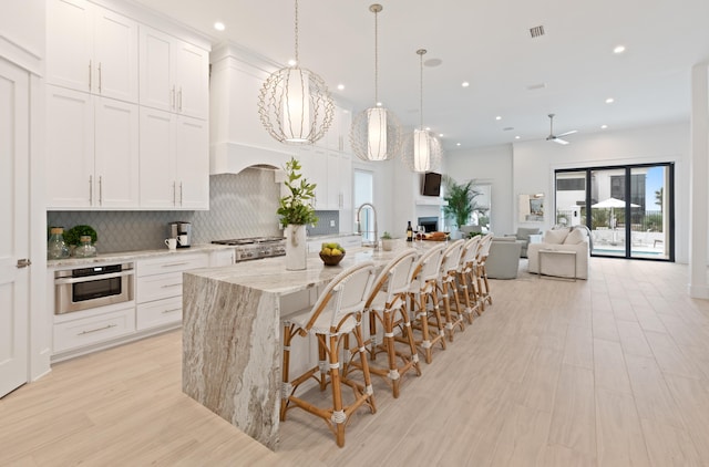 kitchen with light stone countertops, white cabinetry, tasteful backsplash, and an island with sink