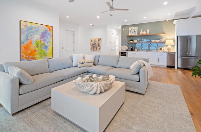 living room featuring ceiling fan, crown molding, and light wood-type flooring