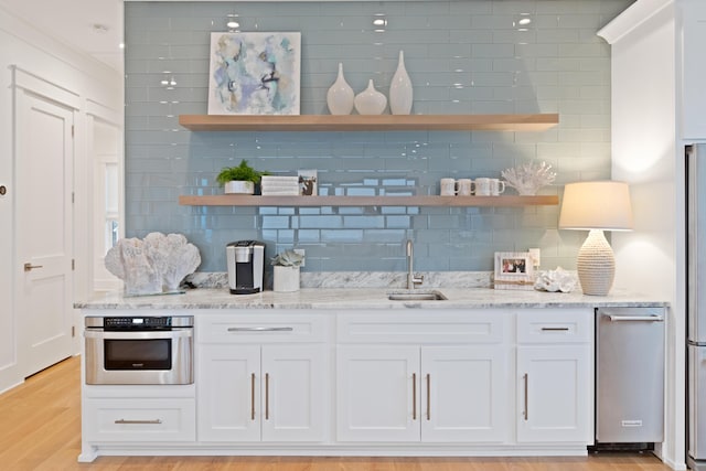 bar with white cabinetry, oven, light stone countertops, light hardwood / wood-style flooring, and sink