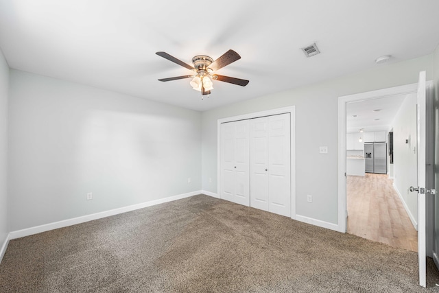 unfurnished bedroom featuring carpet flooring, a closet, ceiling fan, and stainless steel refrigerator with ice dispenser