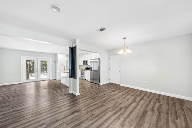 unfurnished living room with dark wood-type flooring, french doors, and a notable chandelier