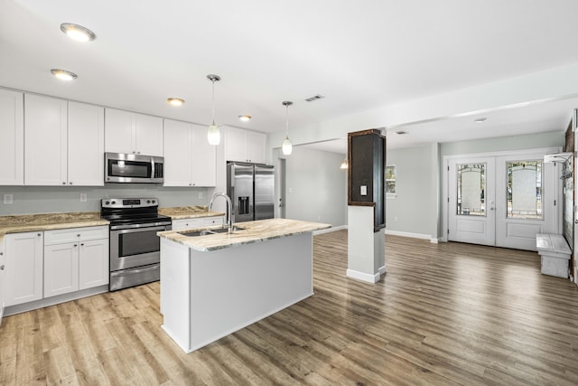 kitchen featuring decorative light fixtures, a center island with sink, white cabinets, and appliances with stainless steel finishes