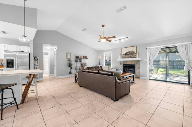 tiled living room with ceiling fan, vaulted ceiling, and a tiled fireplace