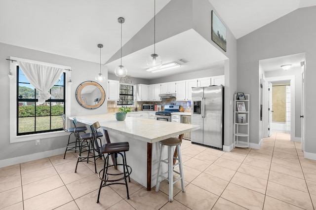 kitchen featuring kitchen peninsula, stainless steel appliances, white cabinets, a breakfast bar area, and pendant lighting