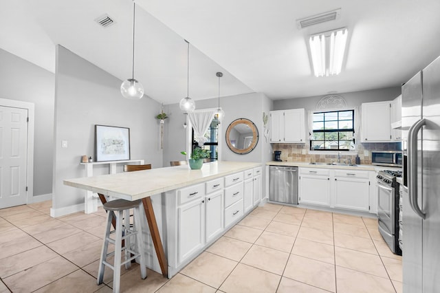 kitchen with a breakfast bar area, stainless steel appliances, pendant lighting, light tile patterned floors, and white cabinetry