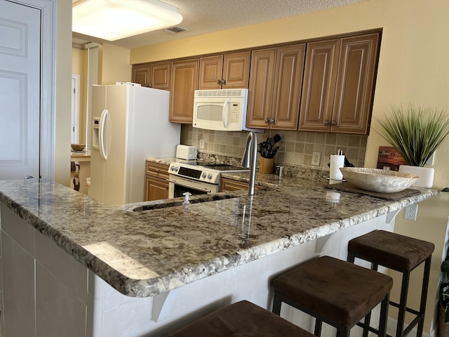 kitchen featuring backsplash, a breakfast bar area, light stone counters, and white appliances