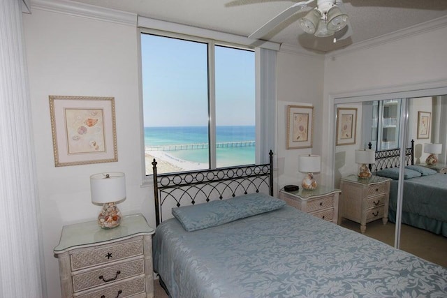 bedroom with ceiling fan, crown molding, a beach view, and a water view