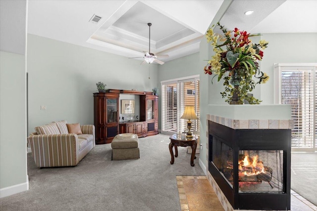 carpeted living room featuring ceiling fan, a raised ceiling, a tile fireplace, and plenty of natural light