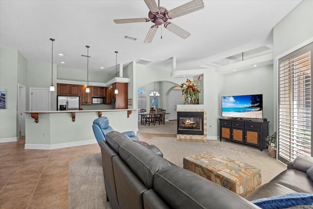 living room with a tiled fireplace, ceiling fan with notable chandelier, and a high ceiling