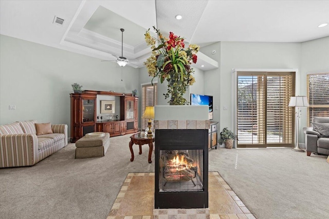 carpeted living room featuring ceiling fan, a raised ceiling, a towering ceiling, and a fireplace