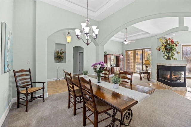 dining room featuring crown molding, a tile fireplace, ceiling fan with notable chandelier, and a tray ceiling