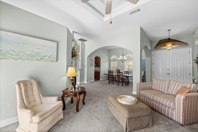 living room with crown molding, ceiling fan with notable chandelier, light colored carpet, and a raised ceiling