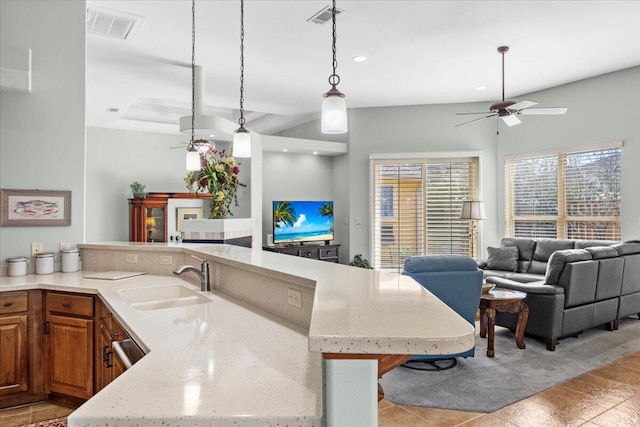 kitchen with ceiling fan, hanging light fixtures, sink, light stone countertops, and a breakfast bar area