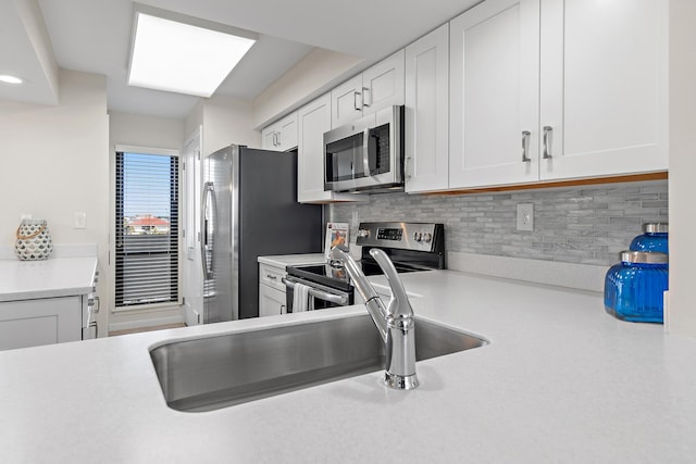 kitchen with appliances with stainless steel finishes, sink, white cabinets, and backsplash