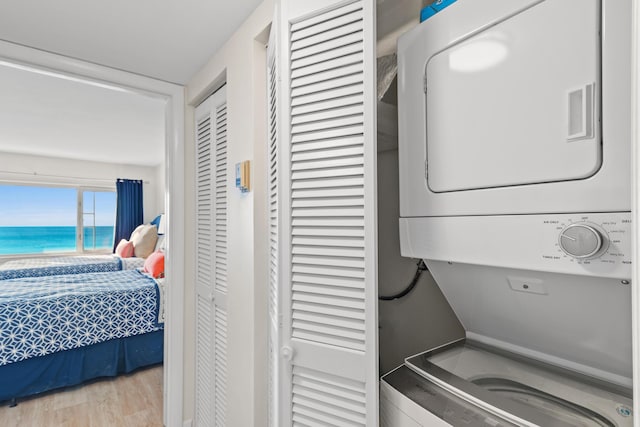 laundry room with a water view, stacked washer / drying machine, and light hardwood / wood-style flooring