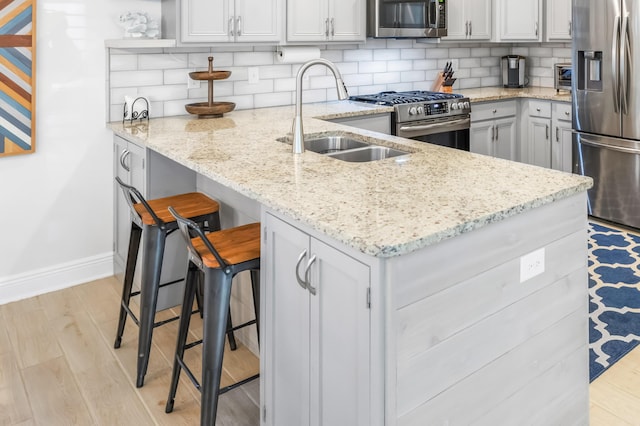 kitchen with light stone countertops, decorative backsplash, light wood-type flooring, sink, and stainless steel appliances