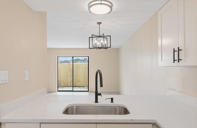 kitchen featuring decorative light fixtures, sink, white cabinets, light stone counters, and an inviting chandelier