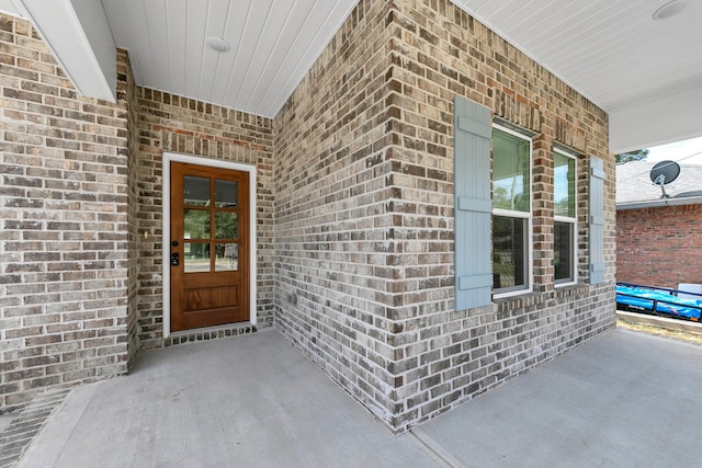 doorway to property featuring covered porch and brick siding