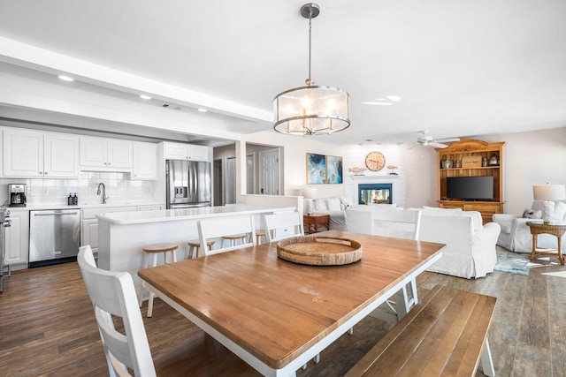 dining space with ceiling fan with notable chandelier, a brick fireplace, dark hardwood / wood-style floors, and sink