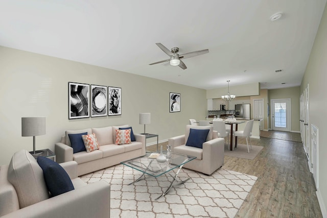 living room with ceiling fan with notable chandelier and light hardwood / wood-style flooring