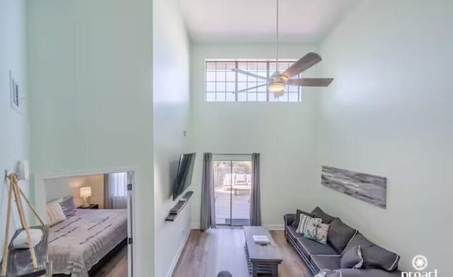 living room with ceiling fan, a wealth of natural light, wood-type flooring, and a towering ceiling