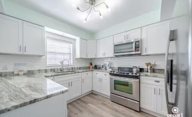 kitchen featuring light stone countertops, white cabinetry, stainless steel appliances, sink, and light wood-type flooring