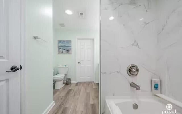 bathroom with hardwood / wood-style floors, toilet, and bathing tub / shower combination