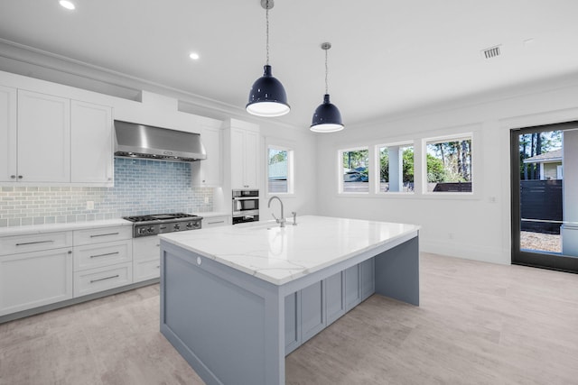 kitchen with a kitchen island with sink, white cabinets, light stone countertops, and wall chimney exhaust hood