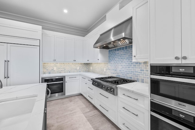 kitchen featuring stainless steel appliances, white cabinetry, light stone counters, and wall chimney exhaust hood