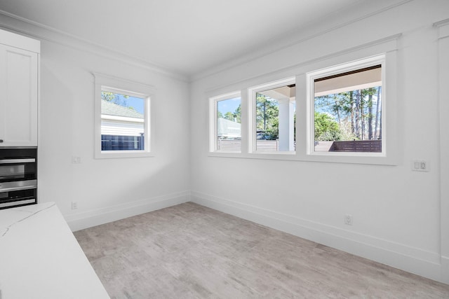 spare room featuring crown molding, light hardwood / wood-style flooring, and a wealth of natural light