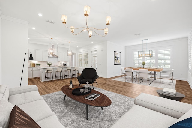 living room with a notable chandelier, ornamental molding, and light wood-type flooring