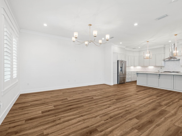 kitchen featuring white cabinetry, wall chimney range hood, a notable chandelier, and high quality fridge