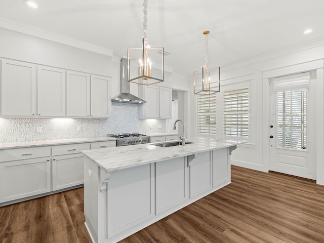 kitchen featuring pendant lighting, sink, white cabinets, a center island with sink, and wall chimney exhaust hood