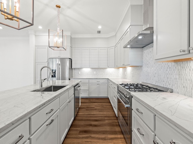 kitchen with wall chimney range hood, sink, hanging light fixtures, high end appliances, and white cabinets