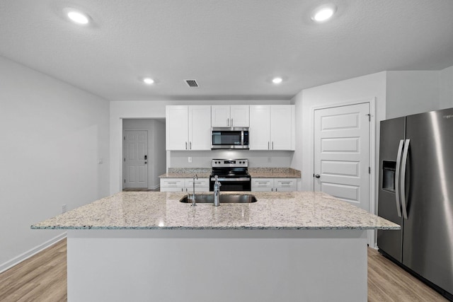 kitchen with light stone countertops, appliances with stainless steel finishes, light hardwood / wood-style flooring, white cabinetry, and a center island with sink