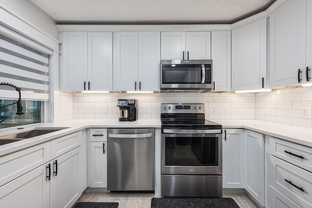 kitchen featuring a textured ceiling, white cabinets, stainless steel appliances, tasteful backsplash, and sink