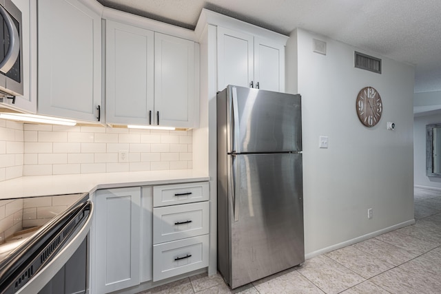 kitchen with white cabinets, light tile patterned floors, a textured ceiling, decorative backsplash, and stainless steel appliances