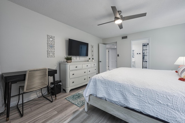 bedroom featuring light wood-type flooring, a textured ceiling, ceiling fan, and ensuite bathroom