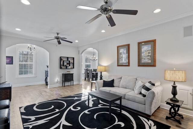 living room with ceiling fan with notable chandelier, ornamental molding, and hardwood / wood-style floors